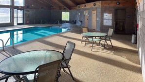 An indoor swimming pool with a tiled floor, wooden ceiling beams, and a glass table with chairs. - Motel 6 Norway, MI (Norway)