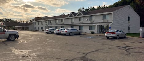 A motel with a parking lot, several cars parked, and a building with a flat roof and multiple windows.