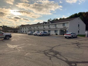 Un motel con estacionamiento, varios autos estacionados, y un edificio de techo plano y múltiples ventanas.