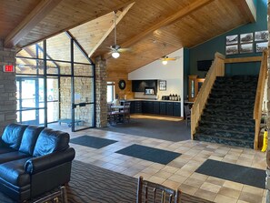 Un hall d’entrée spacieux avec un canapé en cuir, une cheminée en pierre, un coin cuisine et un escalier.