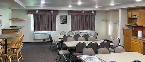 A conference room with a long table, multiple chairs, an air conditioning unit, and a kitchenette area.
