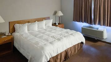 Habitación de hotel con una cama grande, una mesita de noche con lámpara, una mesita auxiliar y un equipo de aire acondicionado.