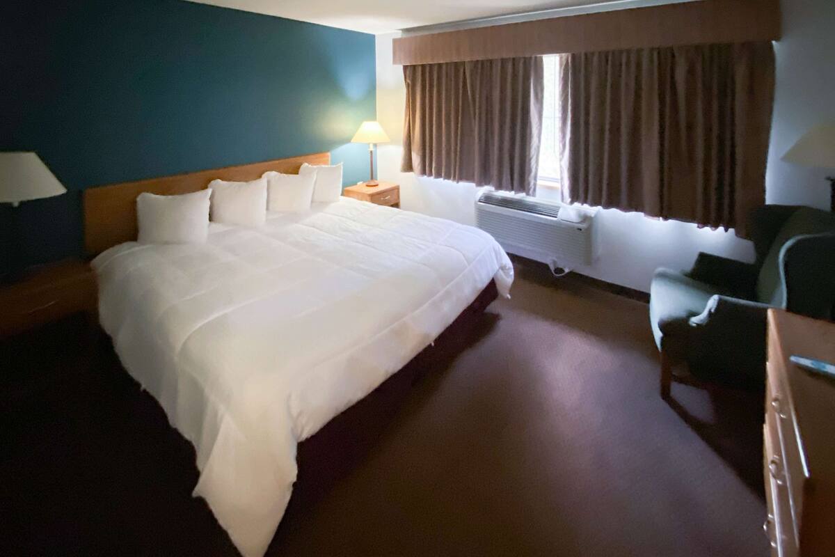 A hotel room with a large bed, a desk with a chair, a lamp, and a window with curtains.