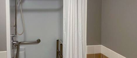 A shower area with a grab bar, a showerhead, and a curtain.
