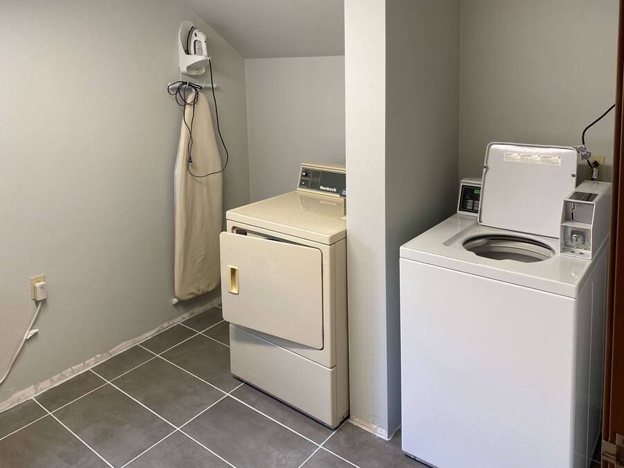 A laundry room with a front-loading washer and dryer, a drying rack, and a power outlet.