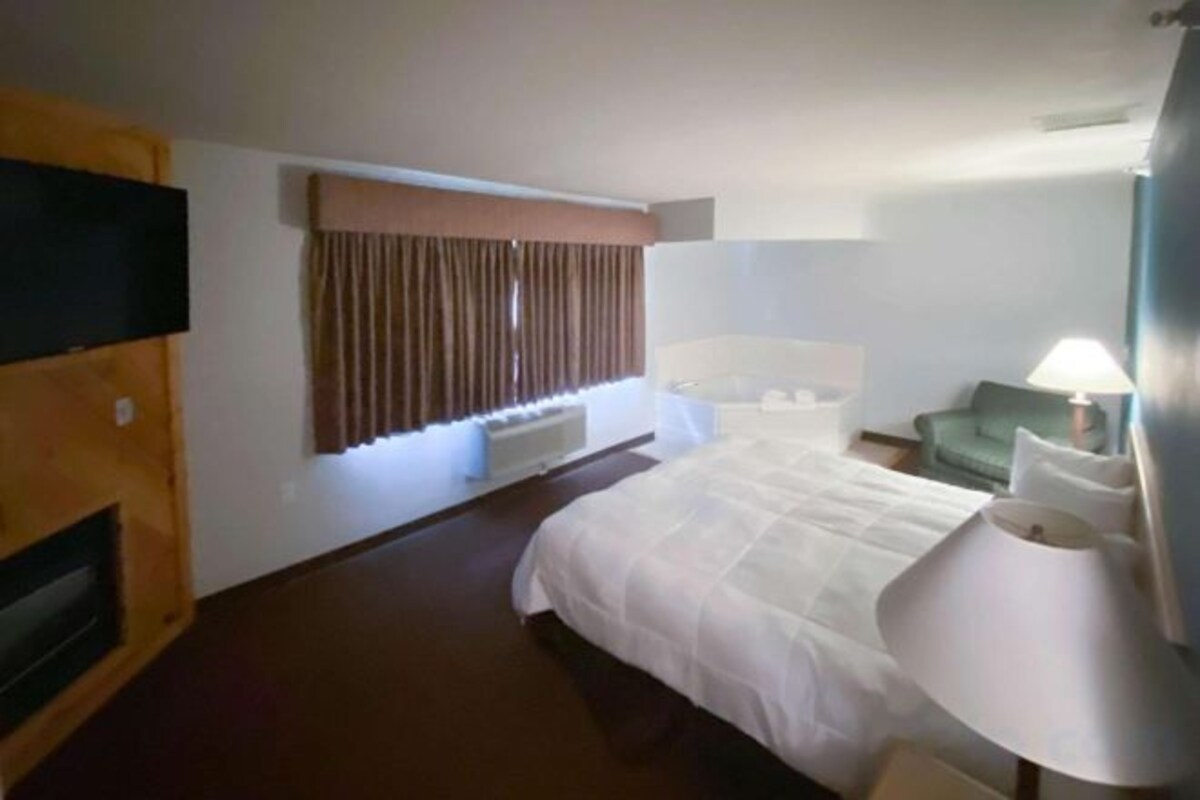 A hotel room with a bed, a television, a desk, a chair, and a window with curtains.