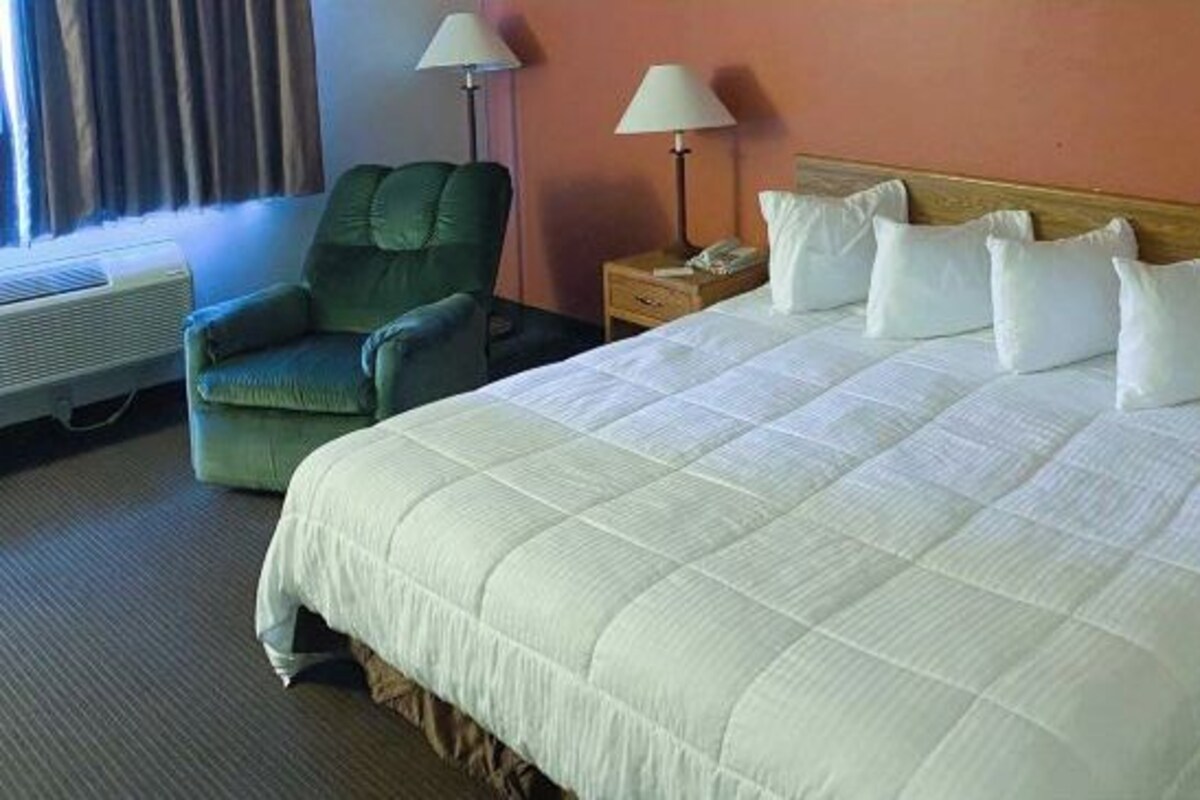 A hotel room with a large bed, a green armchair, two bedside lamps, and a window with curtains.