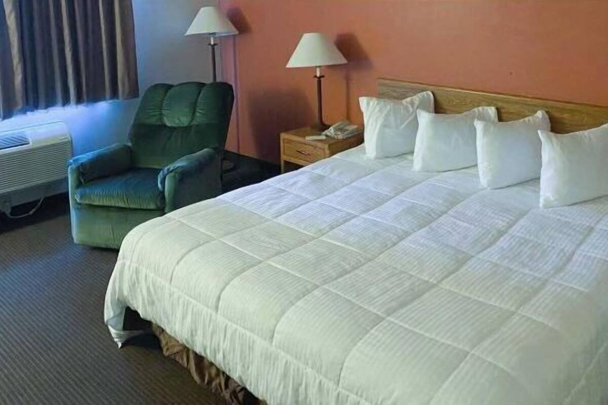 A hotel room with a large bed, a green armchair, two bedside lamps, and a window with curtains.