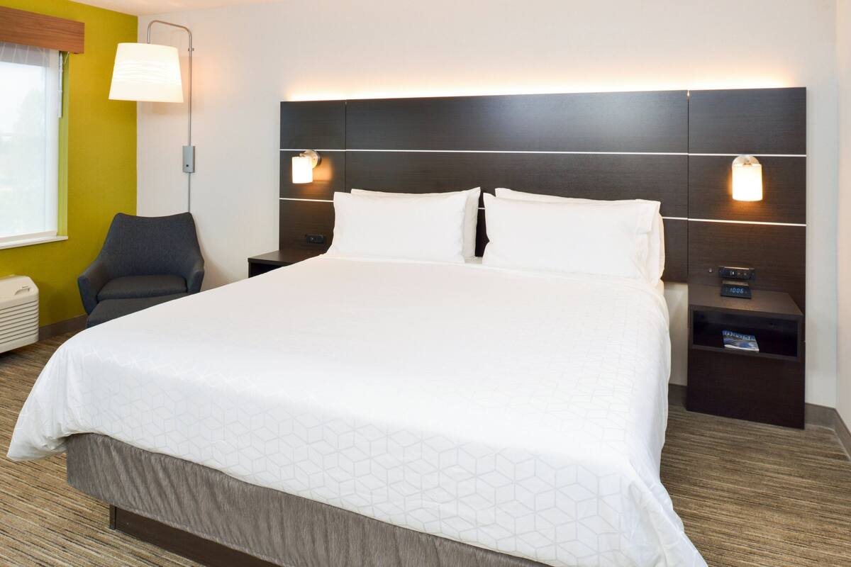 Une chambre d’hôtel avec un grand lit, une table de chevet avec une lampe et une chaise.