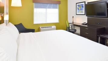 Quarto de hotel com cama, secretária, cadeira, televisão e janela com persianas.