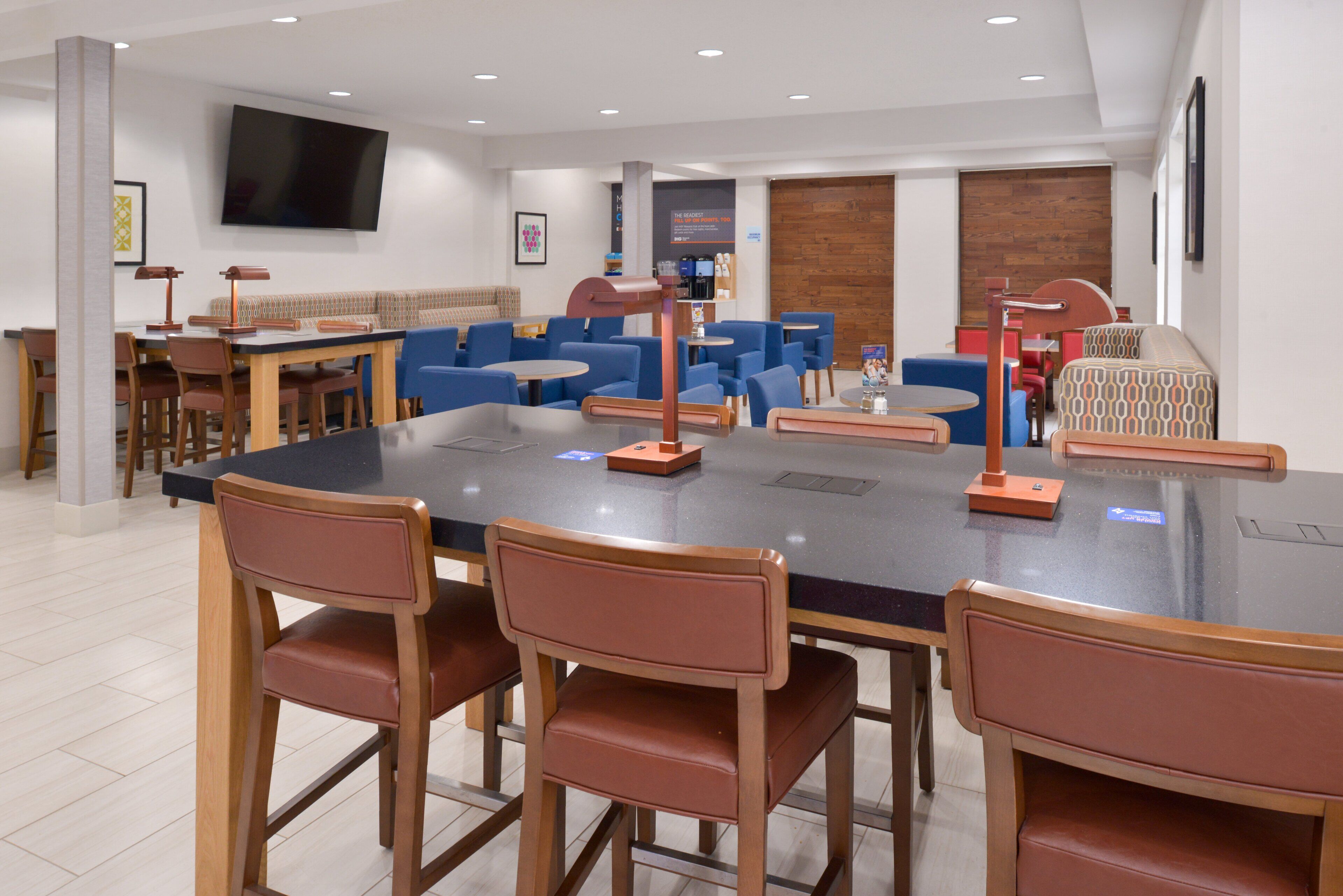 Une salle de réunion moderne dotée d’une grande table ovale, de plusieurs chaises bleues et brunes, d’un téléviseur à écran plat et d’un mur décoratif en bois.