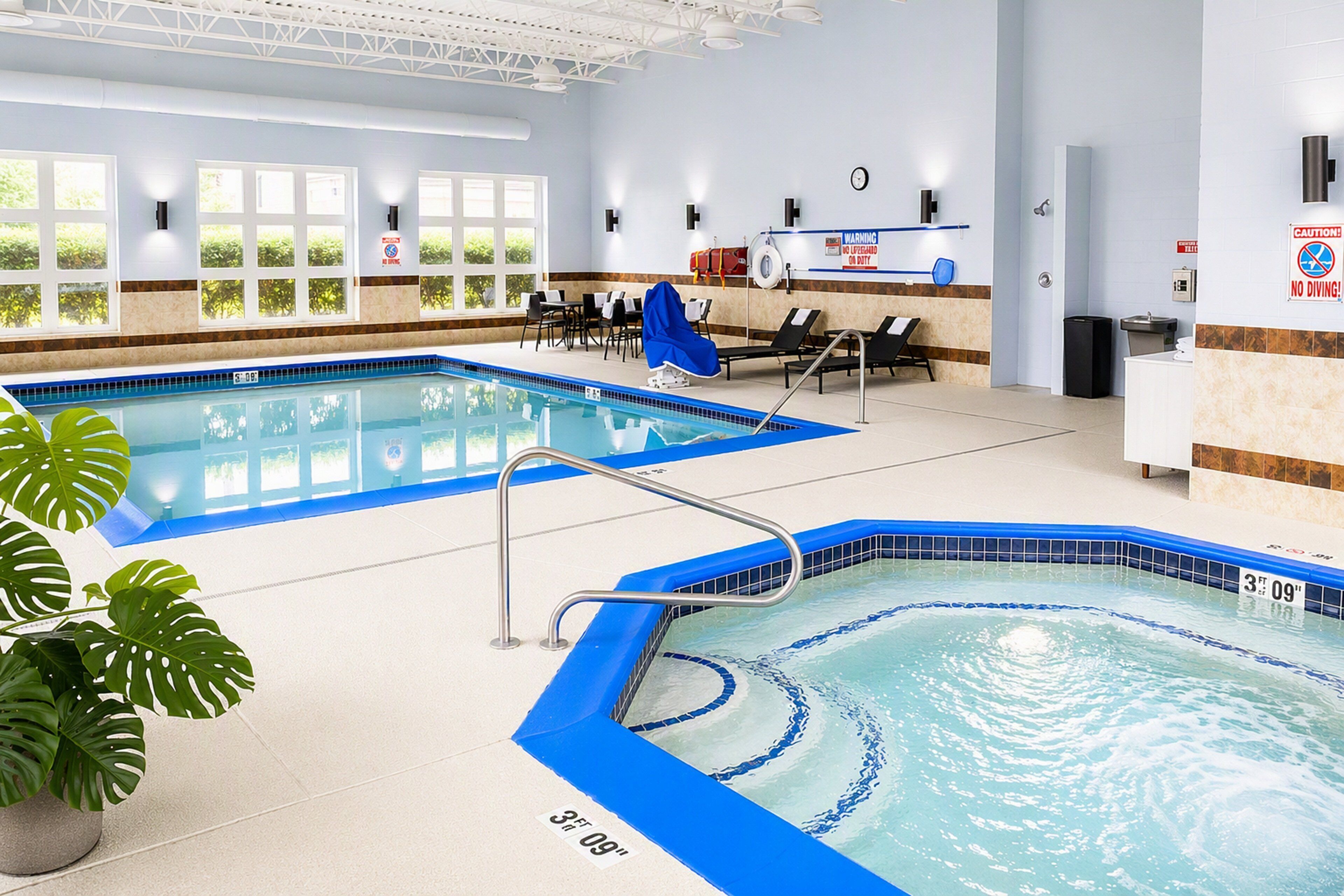 An indoor swimming pool with clear water, a lifeguard chair, and a sign indicating a depth of 3 feet 9 inches.