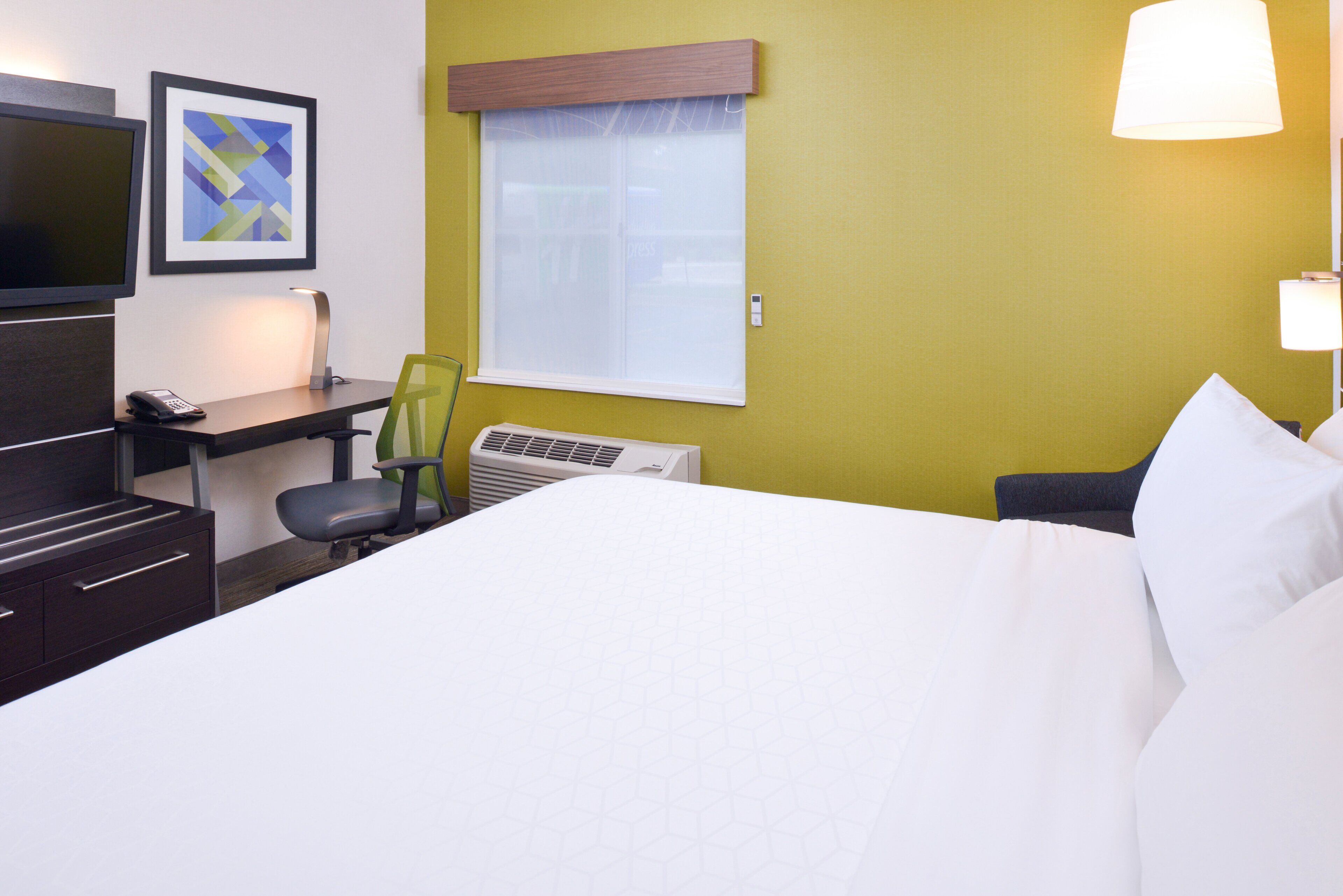 A hotel room with a bed, desk, chair, TV, and window.