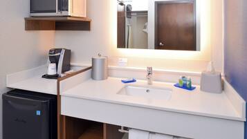 A modern bathroom with a microwave, coffee machine, sink, and a small refrigerator.