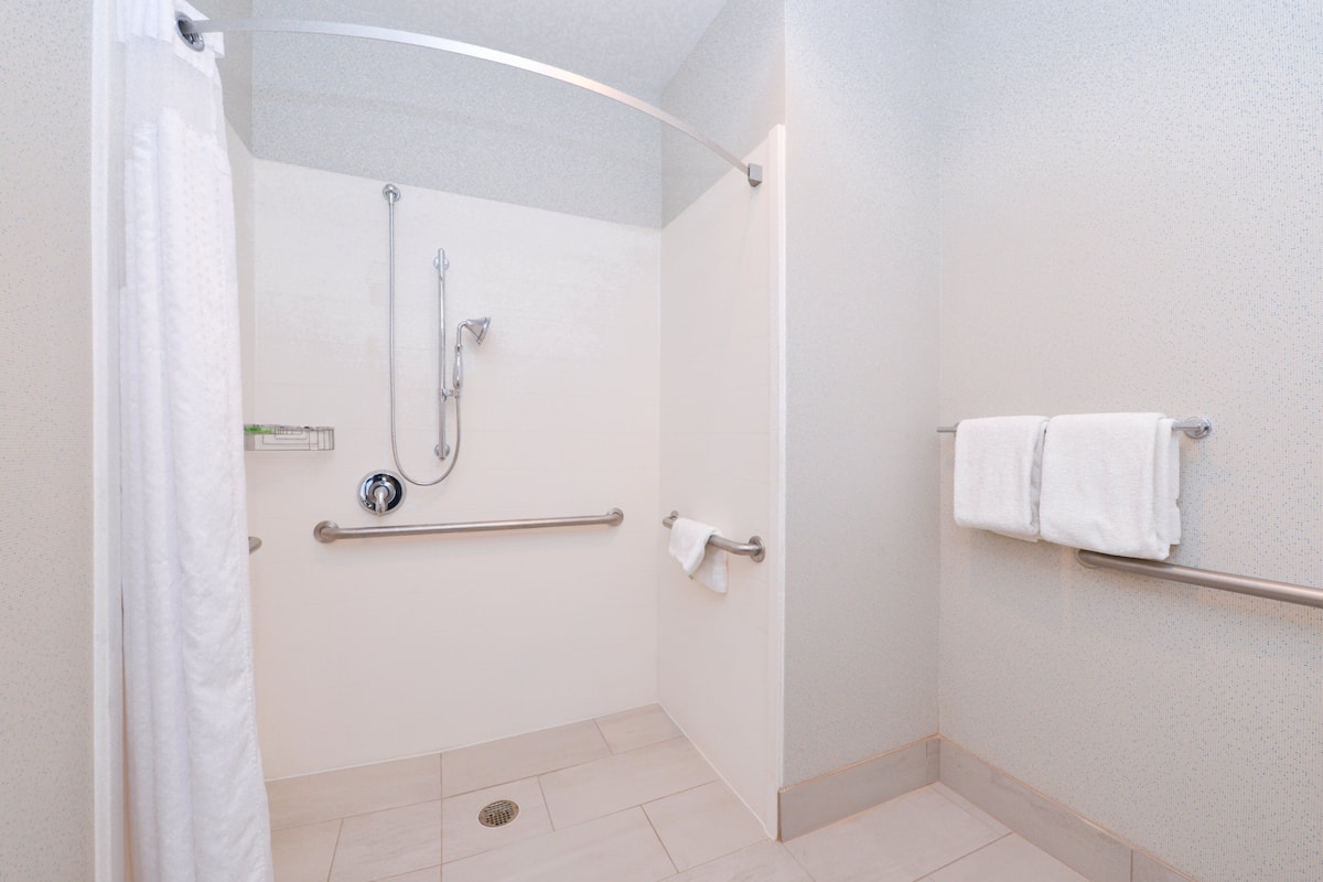 Une douche accessible aux personnes en fauteuil roulant, équipée de barres d’appui, d’un sèche-mains et d’un porte-serviettes.