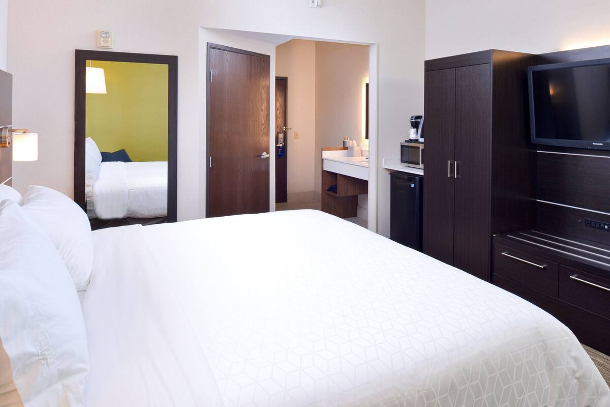 Une chambre d’hôtel avec un grand lit, une télévision, un bureau avec une chaise et une salle de bain visible à travers une porte ouverte.