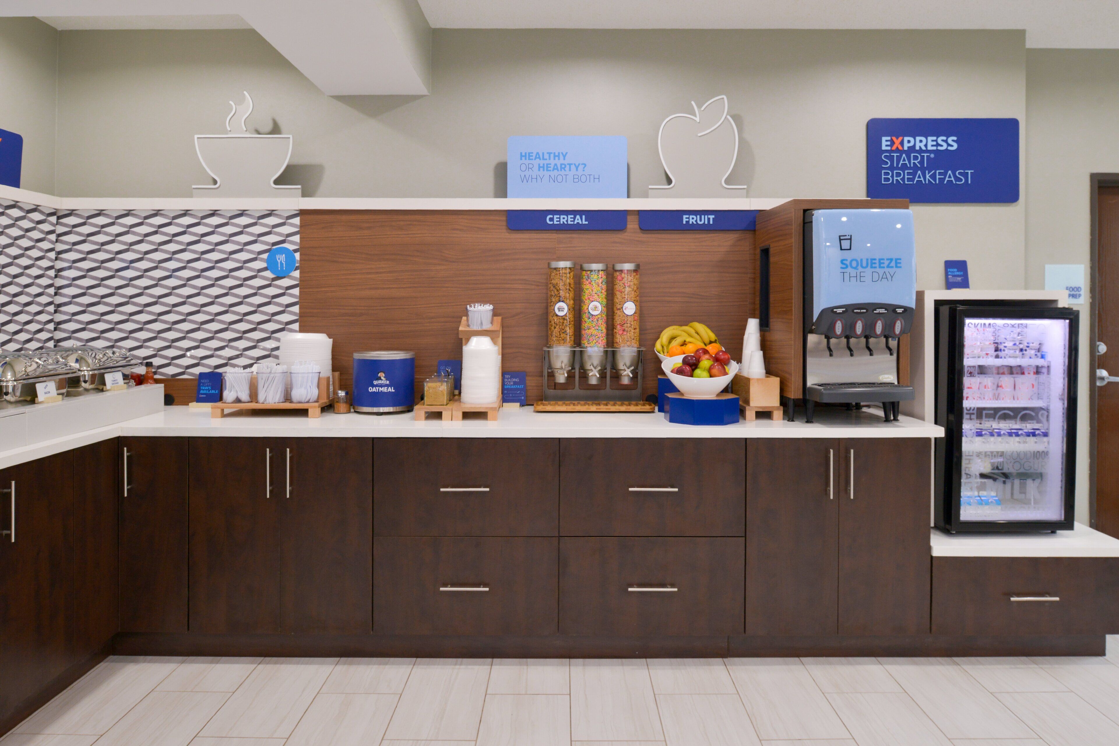 A breakfast area with a cereal and fruit station, a beverage dispenser, and a refrigerator.