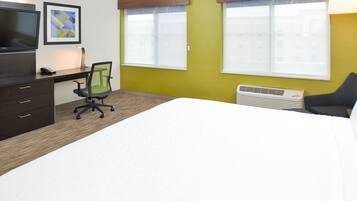 Habitación de hotel con cama, escritorio, silla, televisor y dos ventanas con persianas.