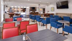 Een moderne hotel lobby met verschillende zithoeken, waaronder rode en blauwe stoelen, en een grote flatscreen televisie aan de muur.