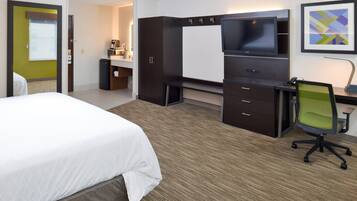 A hotel room with a bed, a desk with a chair, a TV, and a kitchenette.
