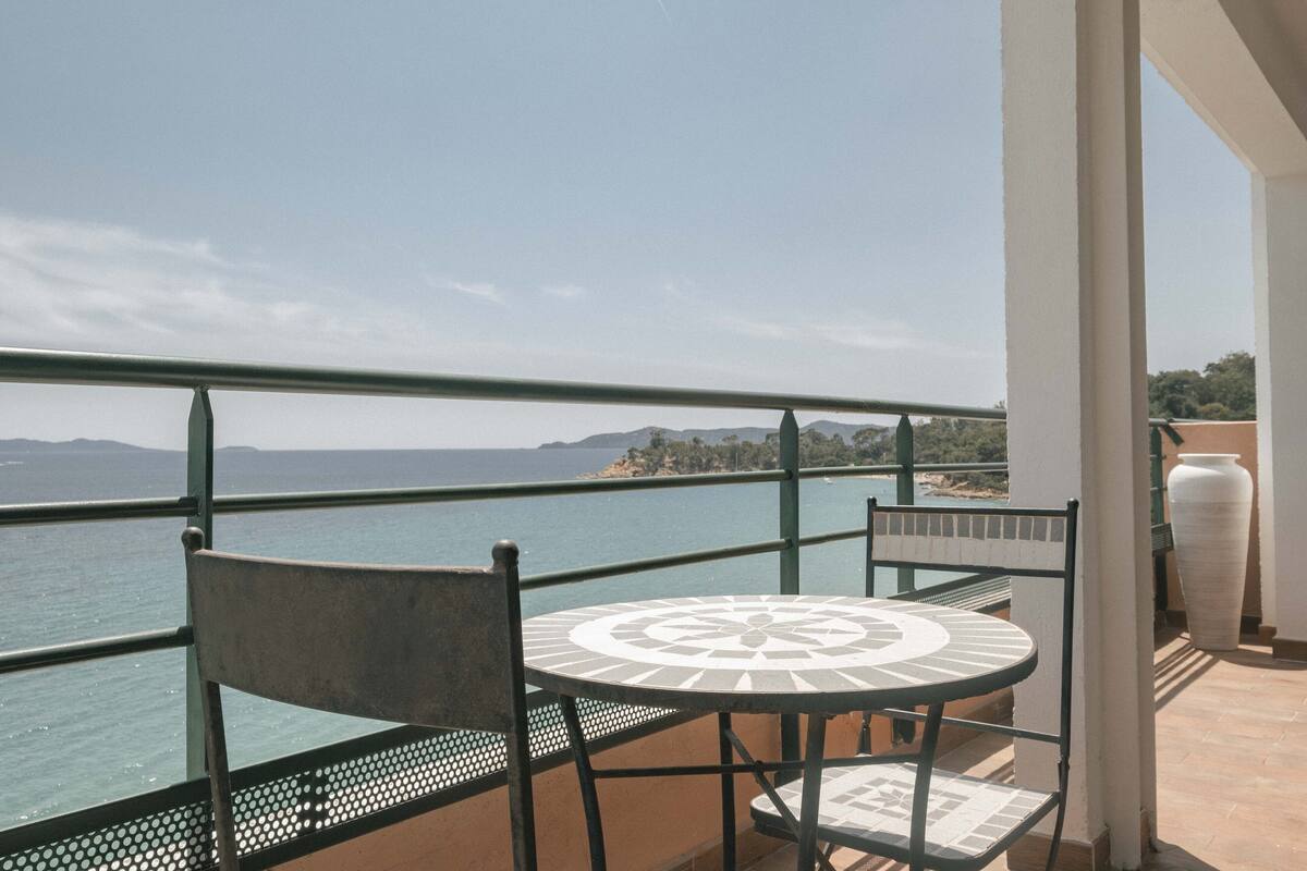 A balcony with a table and chairs overlooking a body of water and distant land.
