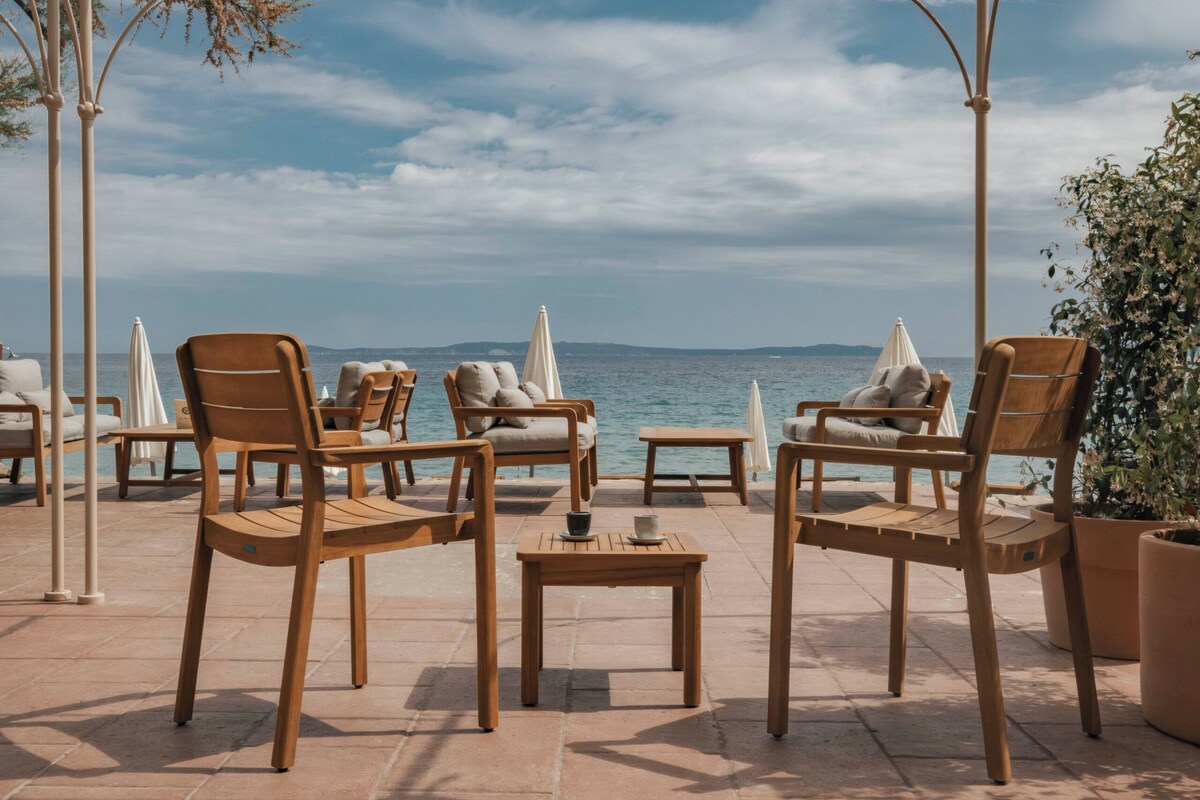 Un espace extérieur aménagé avec des chaises et des tables en bois, donnant sur une étendue d’eau.