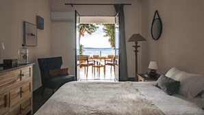 Un dormitorio con cama, una silla, tocador, lámpara y vista al mar a través de una puerta abierta.