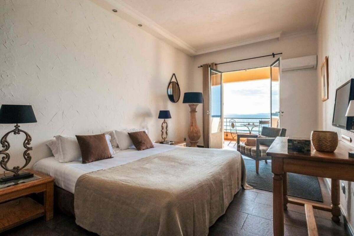 A hotel room with a bed, two bedside tables, a desk, a chair, a TV, and a view of the outdoors.