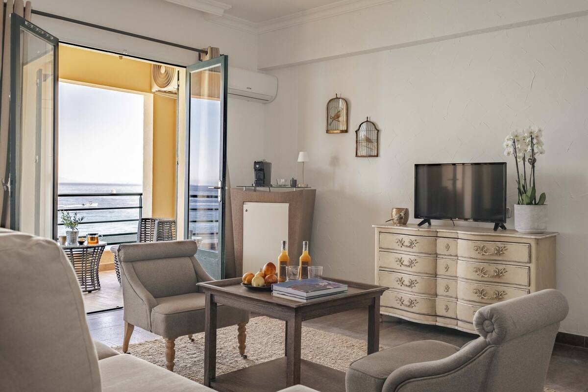 A living room with a sofa, armchairs, a coffee table, a TV, a cabinet, and a balcony with a view.