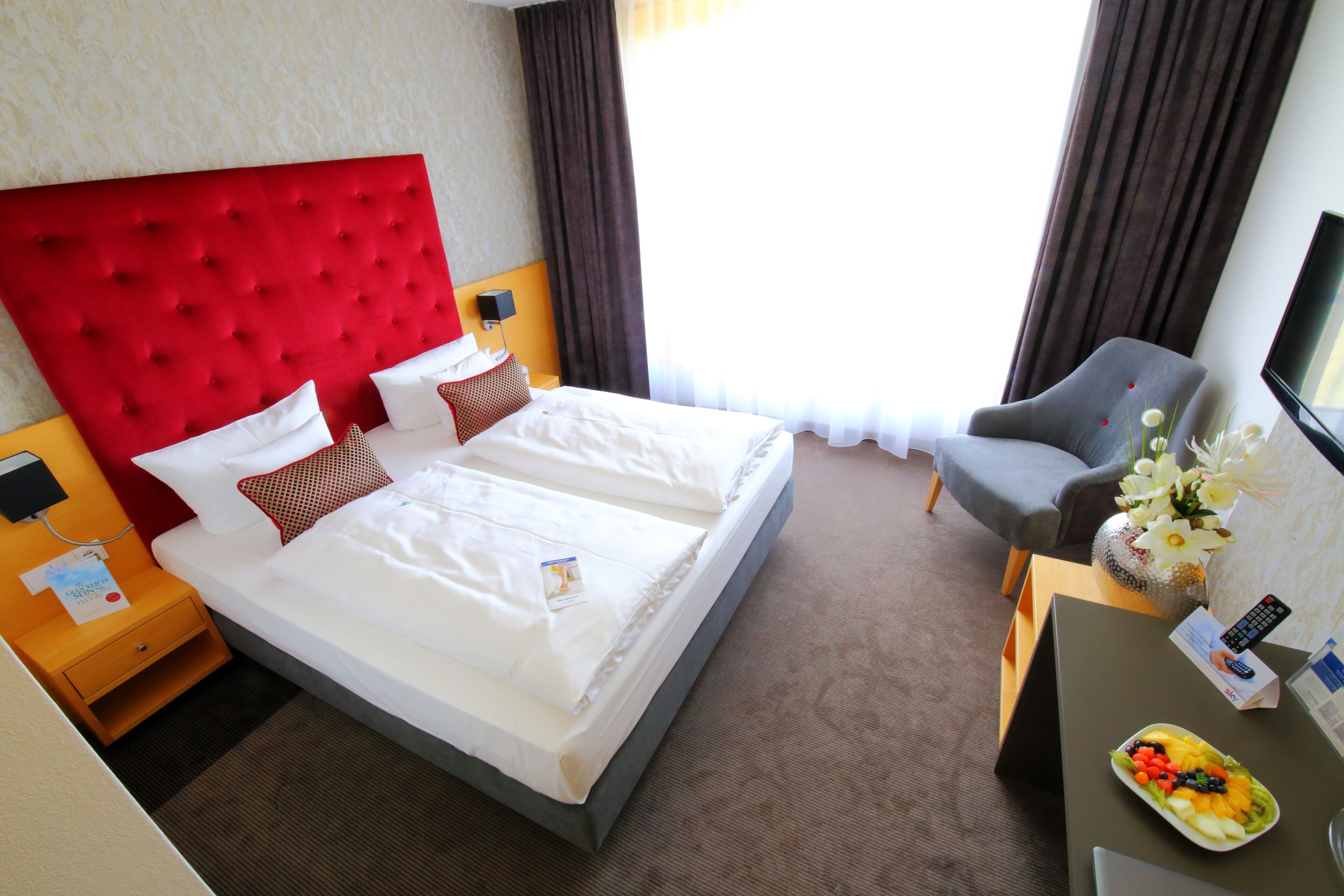 Habitación de hotel con una cama grande, un escritorio con un florero, una silla y un televisor.