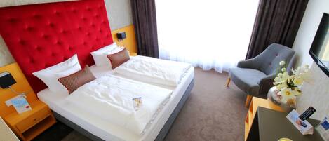 Habitación de hotel con una cama grande, un escritorio con un florero, una silla y un televisor.
