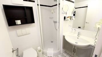 Een moderne badkamer met douche, toilet, wastafel en een zwart kastje met toiletartikelen.