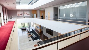 A spacious, multi-level interior with a red carpet, wooden flooring, and a mezzanine with a glass railing.