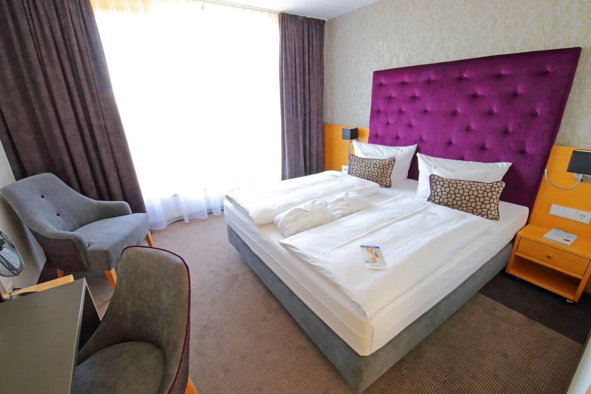 A hotel room with a large bed, a chair, a desk, and a nightstand.