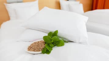 A neatly made bed with white linens and pillows, a bowl of seeds, and a sprig of mint on the bed.