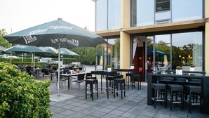 An outdoor seating area with tables and chairs, umbrellas, and a building with large windows.