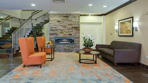 A living room with a stone fireplace, orange chairs, a brown sofa, and a staircase with a railing.