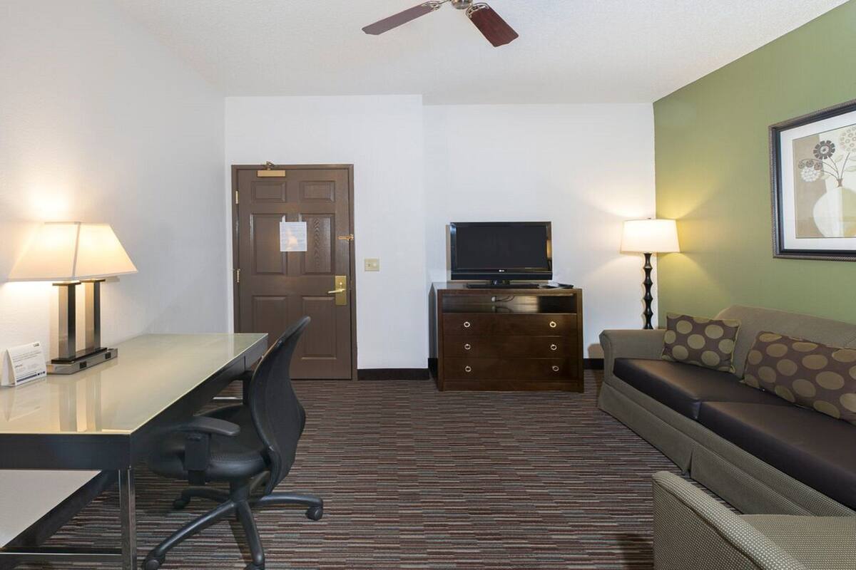 A hotel room with a desk, chair, television, dresser, and sofa.