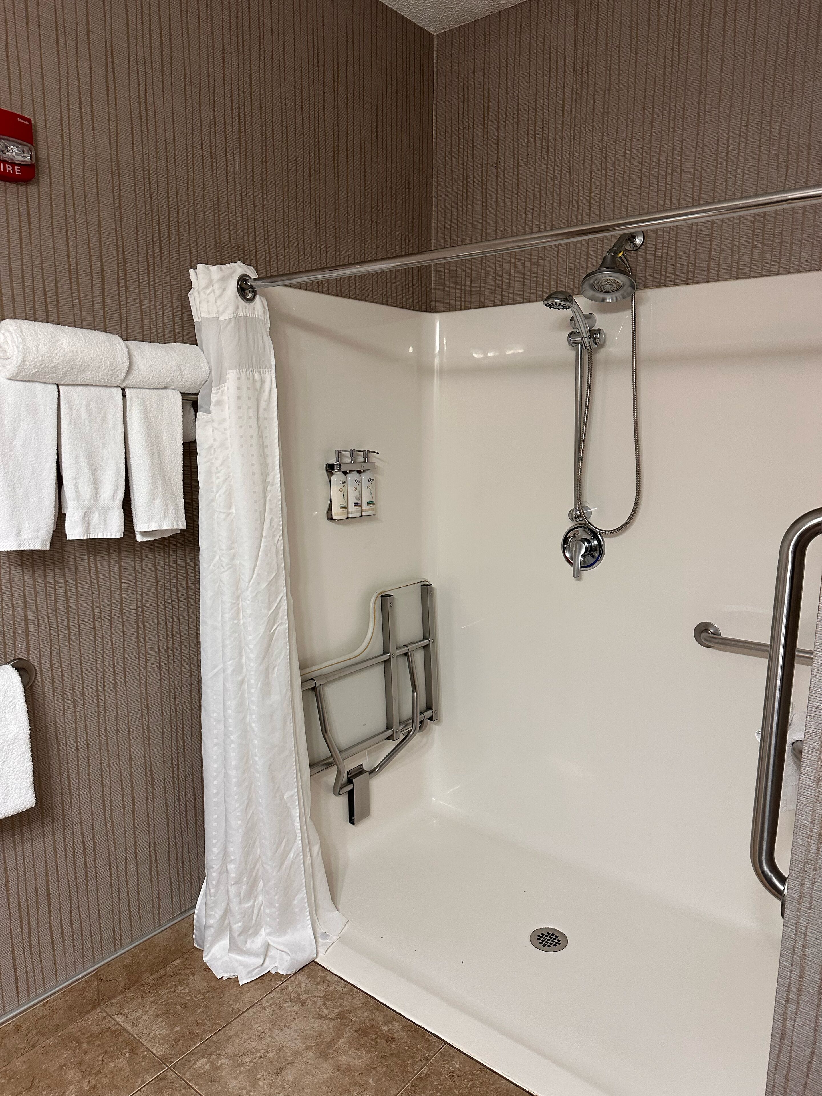 A modern bathroom with a walk-in shower, a towel rack with folded towels, and a set of toiletries.