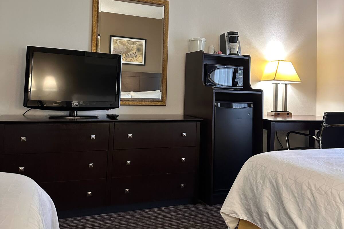 A hotel room with two beds, a television, a desk with a lamp, a coffee maker, and a mirror.