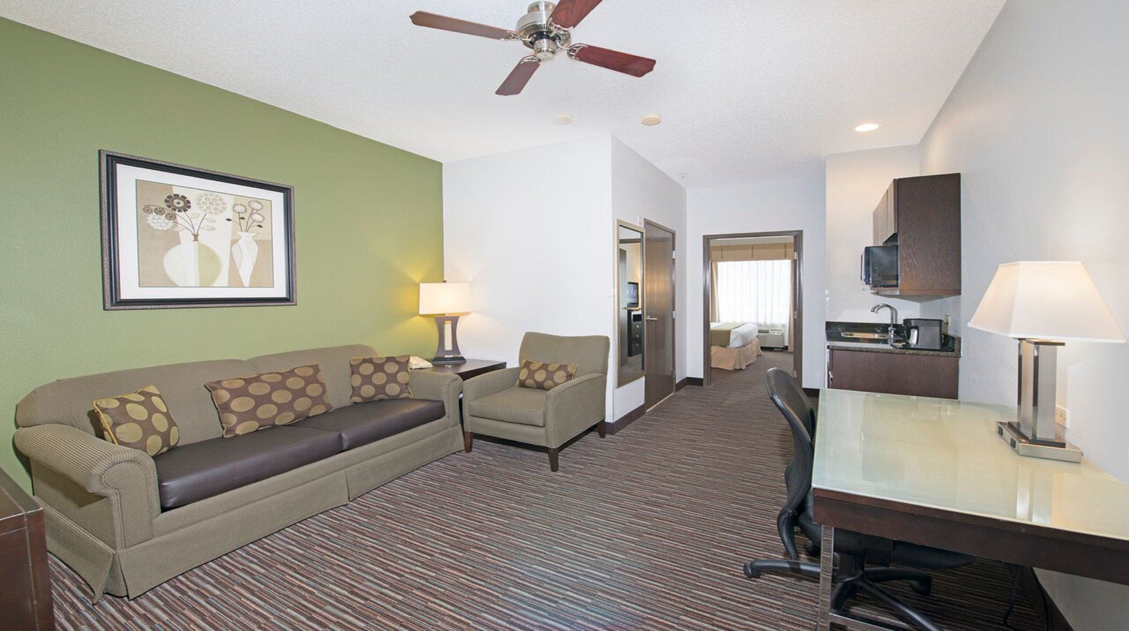 A hotel room with a sofa, armchair, desk, and a ceiling fan.