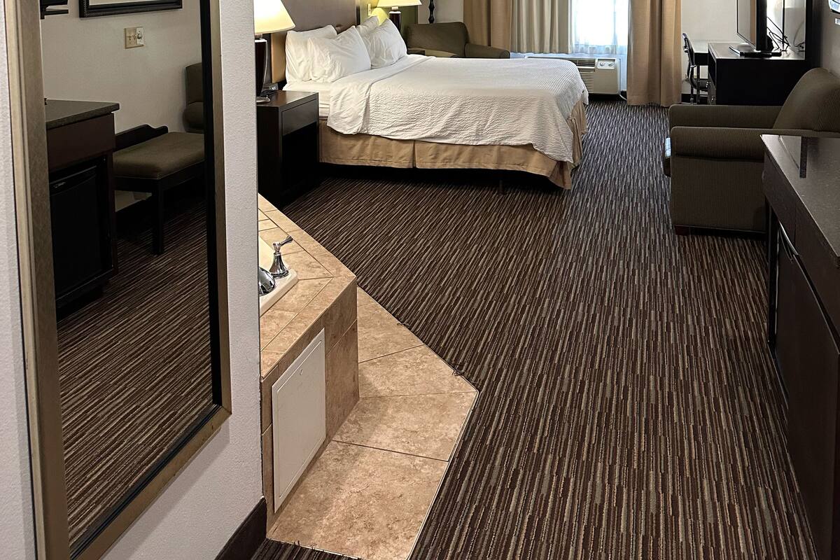 A hotel room with a bed, bedside tables, a desk, a chair, a TV, and a window with curtains.