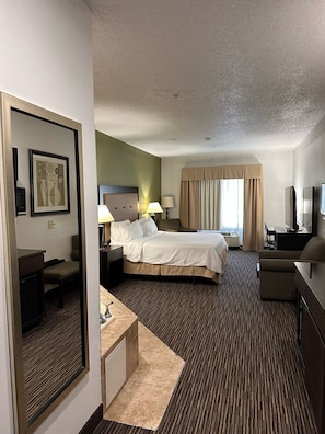 Habitación de hotel con cama, mesitas de noche, escritorio, silla, televisor y ventana con cortinas.