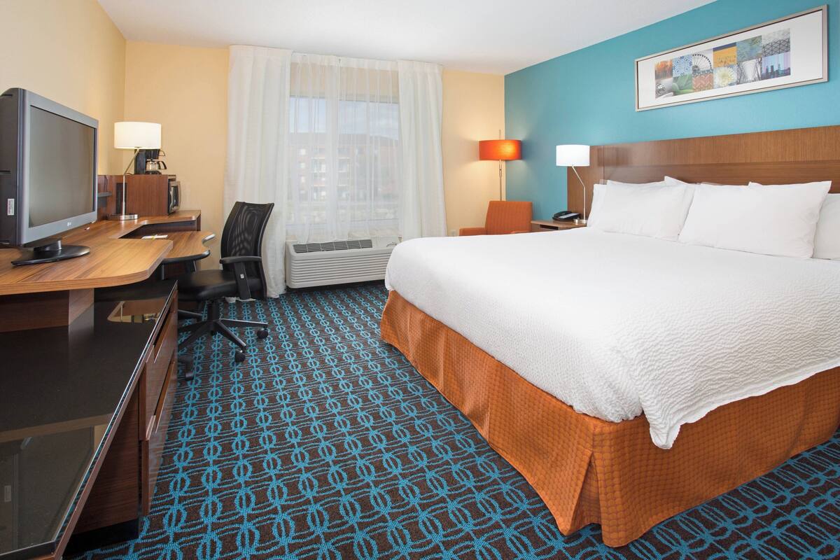 Une chambre d’hôtel avec un grand lit, un bureau avec un ordinateur, une chaise, un appareil de climatisation et une fenêtre avec des rideaux.