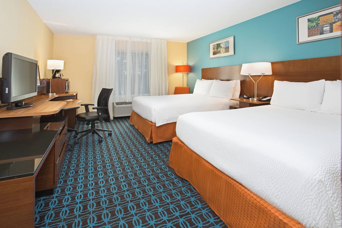 Une chambre d’hôtel avec deux lits, un bureau avec un ordinateur, une chaise et un téléviseur.