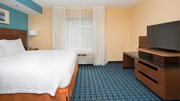A hotel room with a bed, a television, a desk, and a patterned carpet.