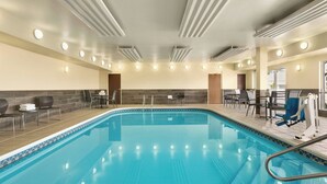A swimming pool with a tiled edge, surrounded by chairs and tables, and a ceiling with recessed lighting.