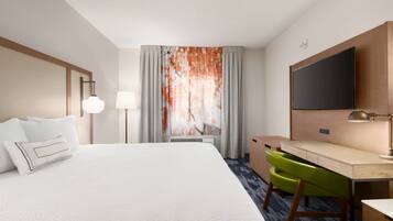 Habitación de hotel con una cama grande, un escritorio, una silla, un televisor de pantalla plana y una ventana con cortinas.