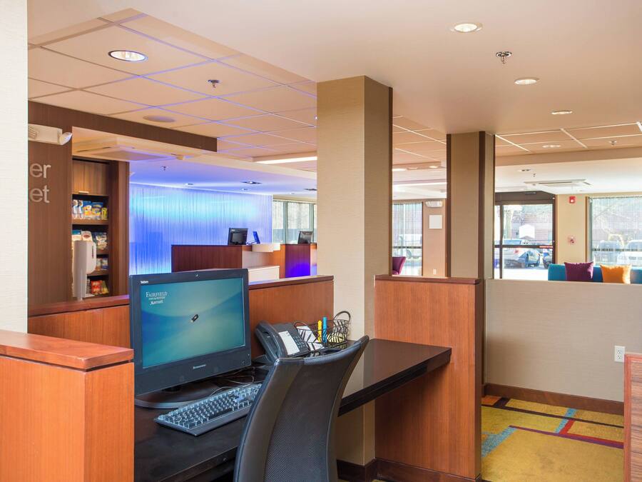 A hotel reception area with a computer desk, a telephone, and a small shelf with items. There is a window with a view of the outside.