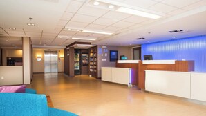 A reception area with a wooden reception desk, a blue wall, and a hallway leading to elevators. - Fairfield by Marriott Inn & Suites Raynham Middleborough/Plymouth (Middleborough)
